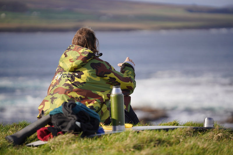 A surfer sat drinking coffee and watching the waves in a dryrobe Advance