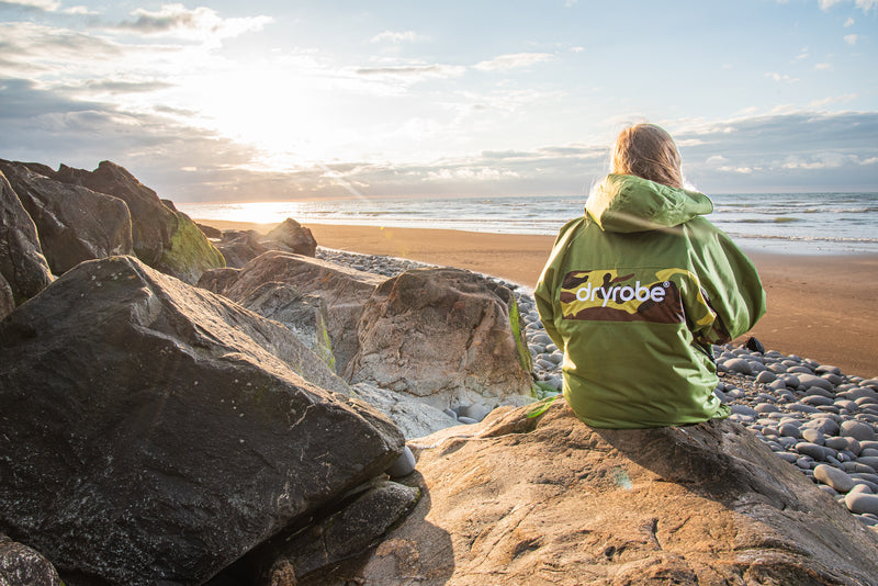 Women sat on the beach watching the sunset in a Forest Green and Camo REMIX range dryrobe Advance