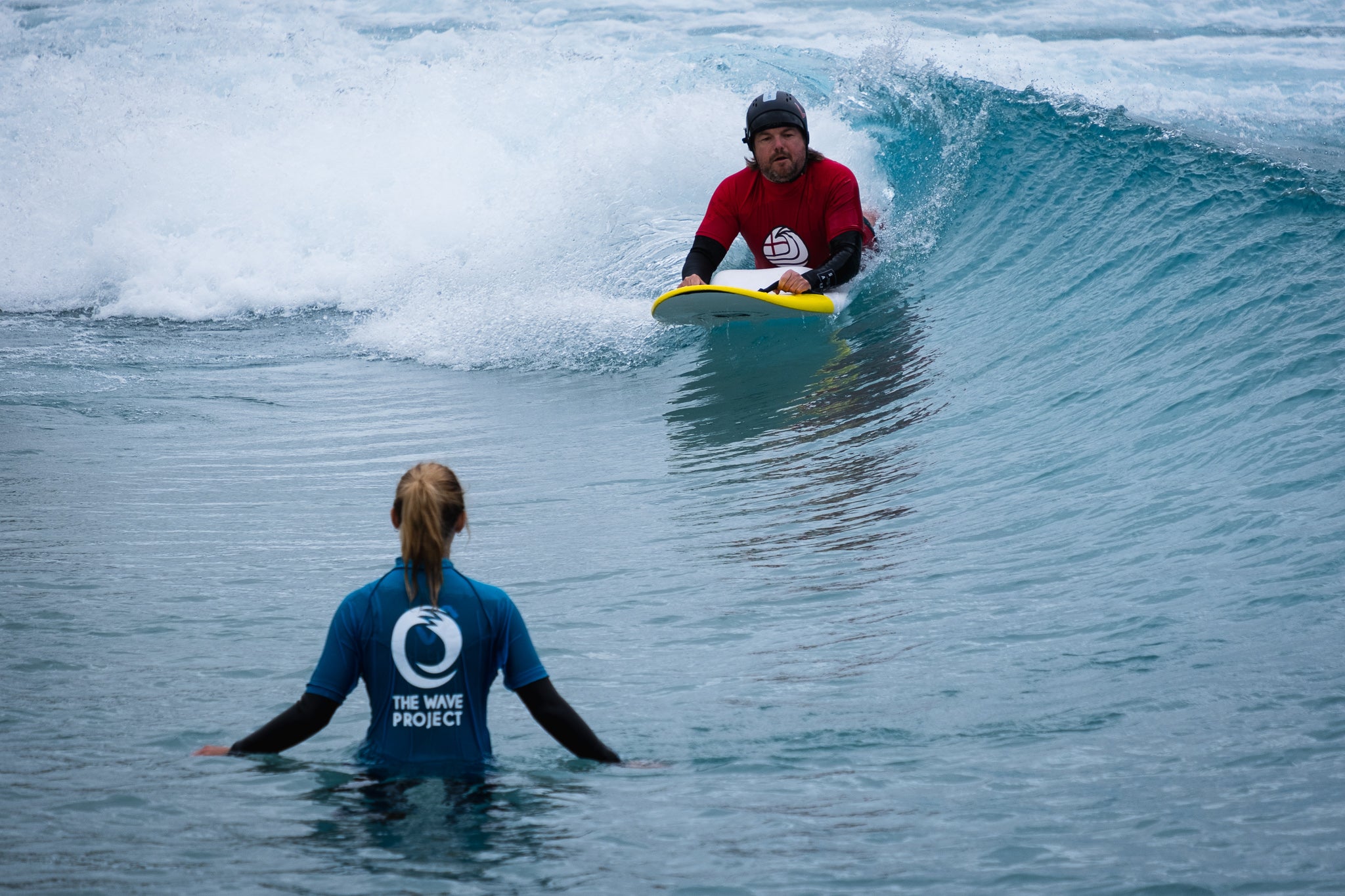 Adaptive surfer Mark Hagger surfing towards a volunteer at The Wave