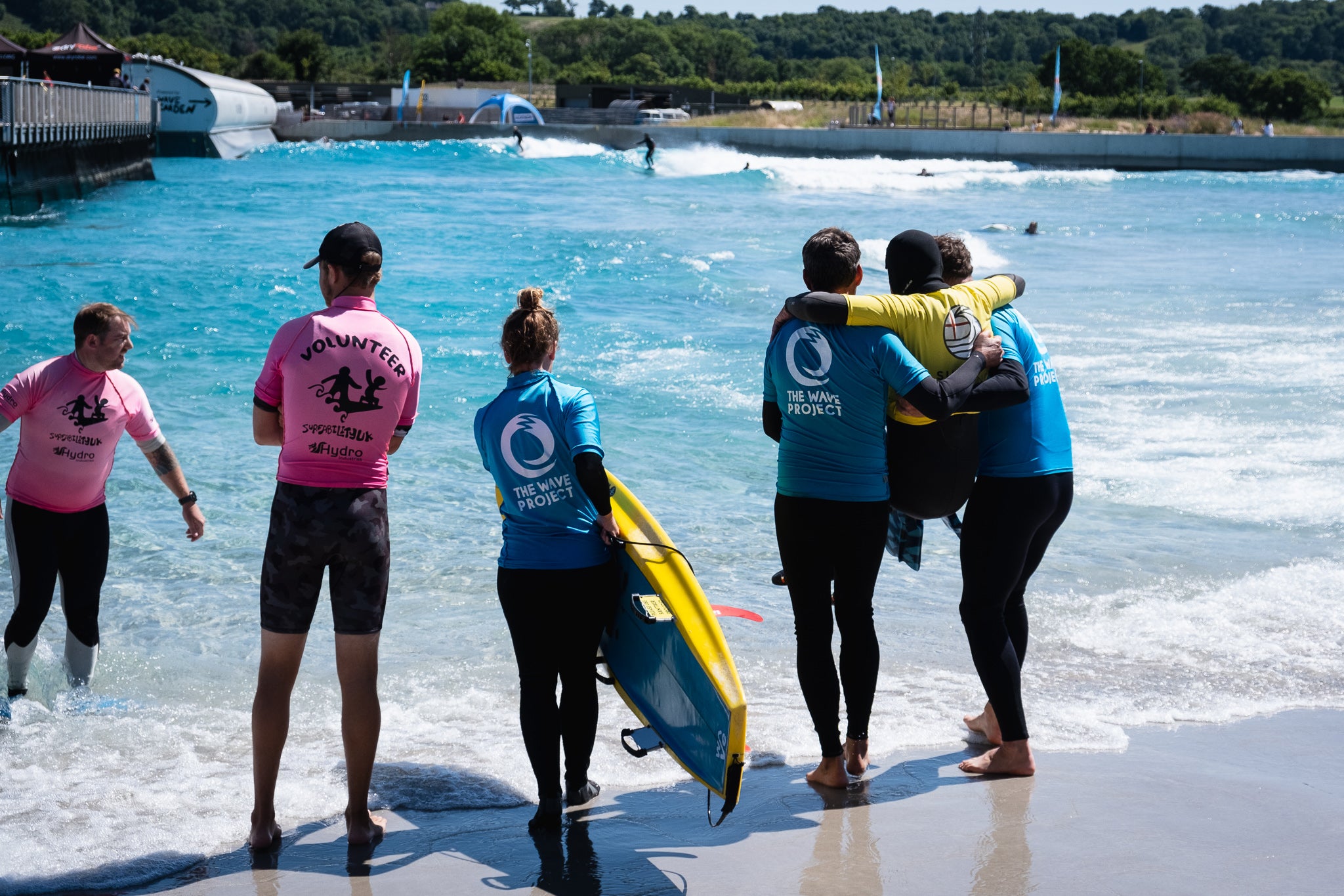 Volunteers carrying an adaptive surfer in to the water at the Wave in Bristol