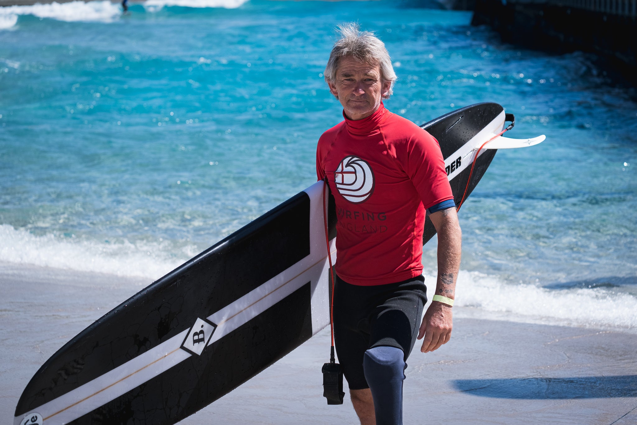 Adaptive Surfer Peg Leg Bennet holding his surfboard in front of a Wave Pool