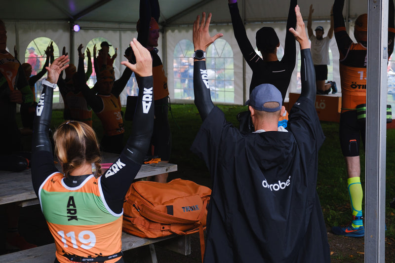 A group of people warming up for a swim run race, one wearing a dryrobe Lite changing robe