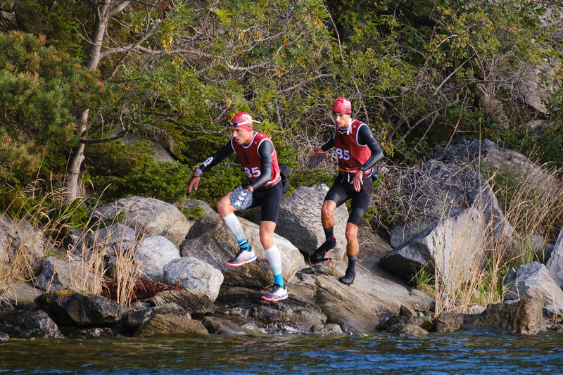 Two swimrunners in red bibs running along the shoreline