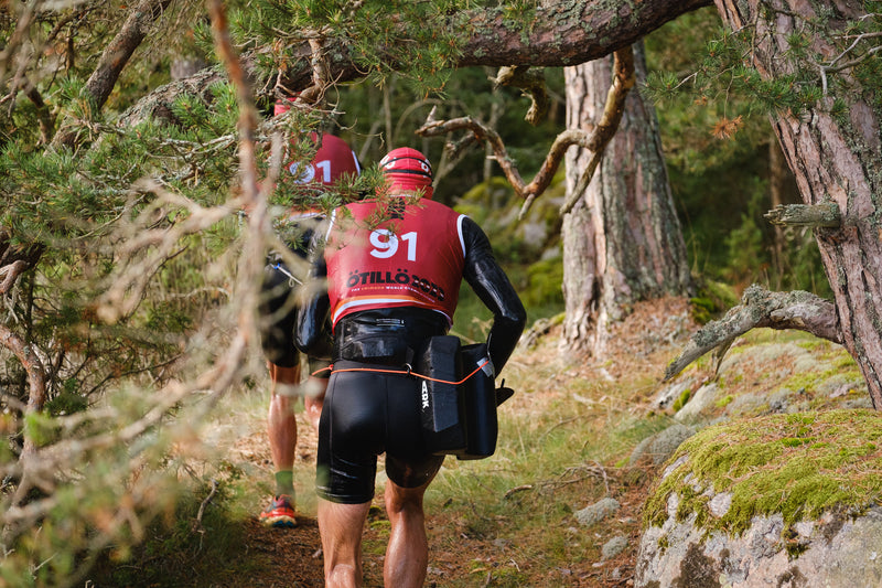 Two swimrunners in red bibs running through a forest