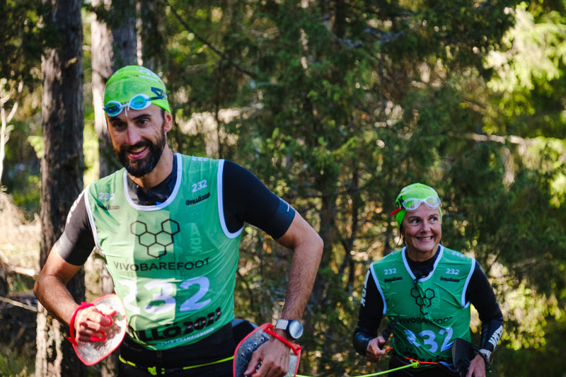 Two smiling swimrunners in green bibs running through woods