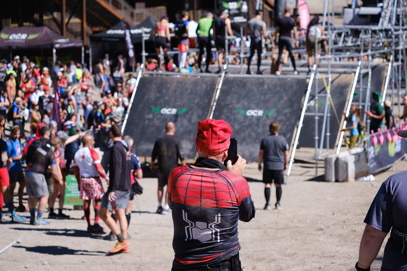 A OCR athlete in a spiderman costume taking a photo of people on an obstacle