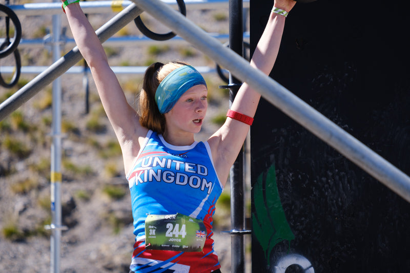 OCR Athlete Libbie Joyce wearing a United Kingdom Jersey and hanging from an obstacle