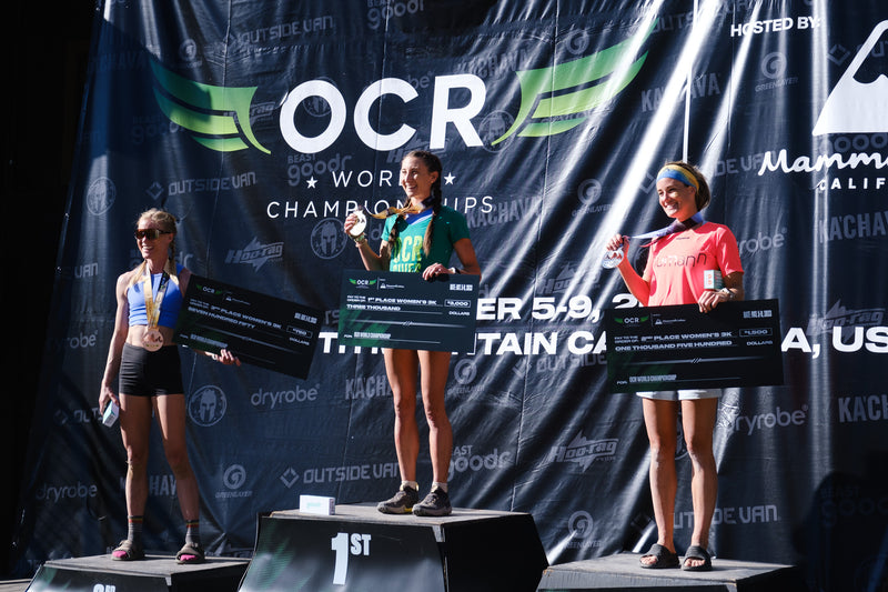 Nicole Mericle, Lindsay Webster and Annie Dube standing on the OCRWC 2023 Podium holding their medals and cheques