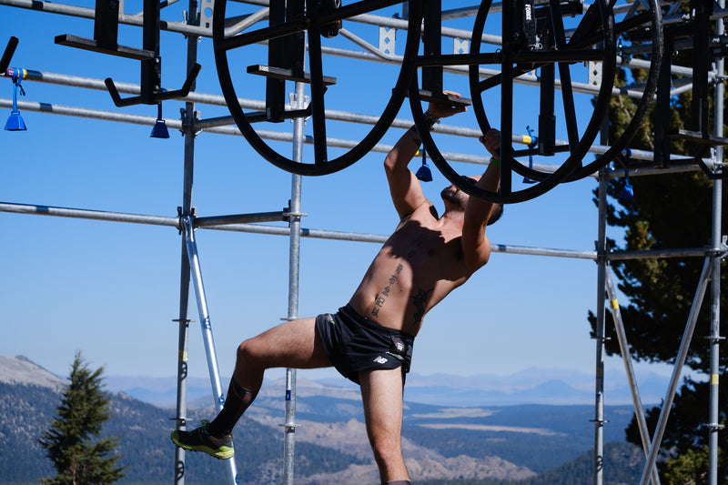 A shirtless man hanging from an obstacle with the sierra nevada mountains in the background