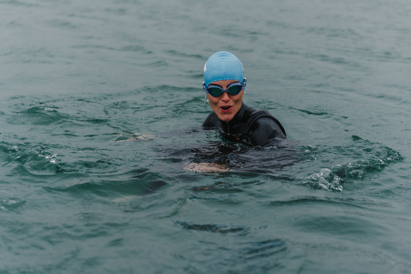 A woman swimming in the sea in a wetsuit, goggles and swimcap