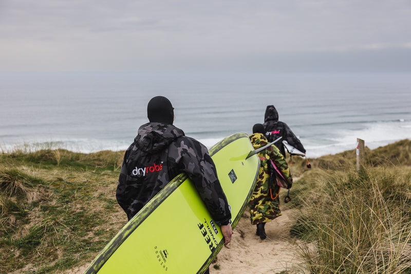 Ben Skinner, Lukas Skinner and Lila Skinner carrying their boards on the beach towards the sea, wearing dryrobes