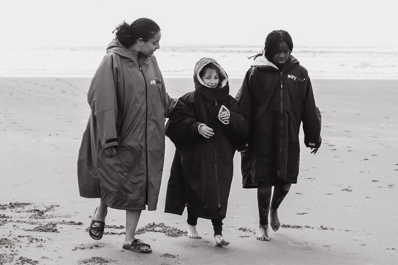 A black and white photo of an adult and two children walking on the beach in change robes 