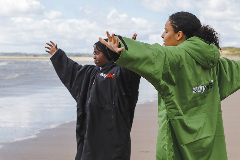 A woman and child stretching their hands out on the beach both wearing dryrobe Advance change robes 