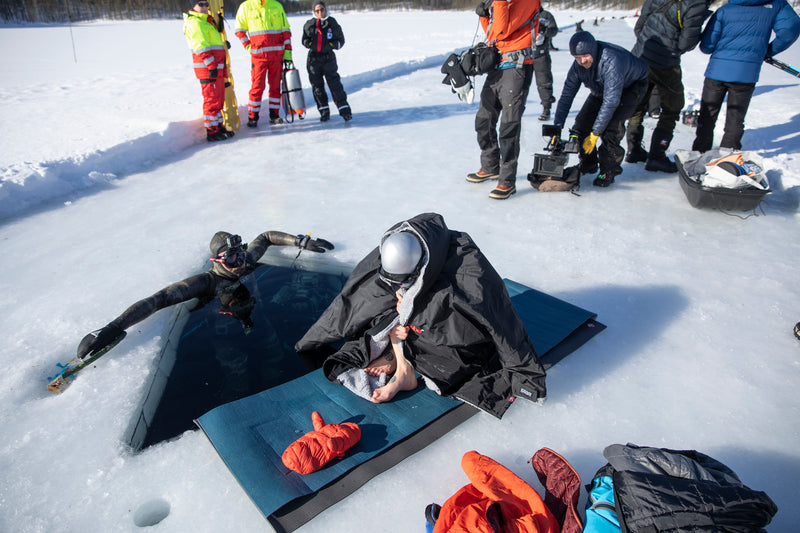 Johanna sat on the ice lake about to dive, head down and wrapped in a dryrobe® 