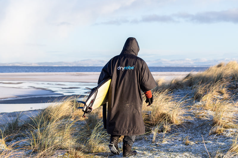 Taz Knight walking in the dunes with surfboard