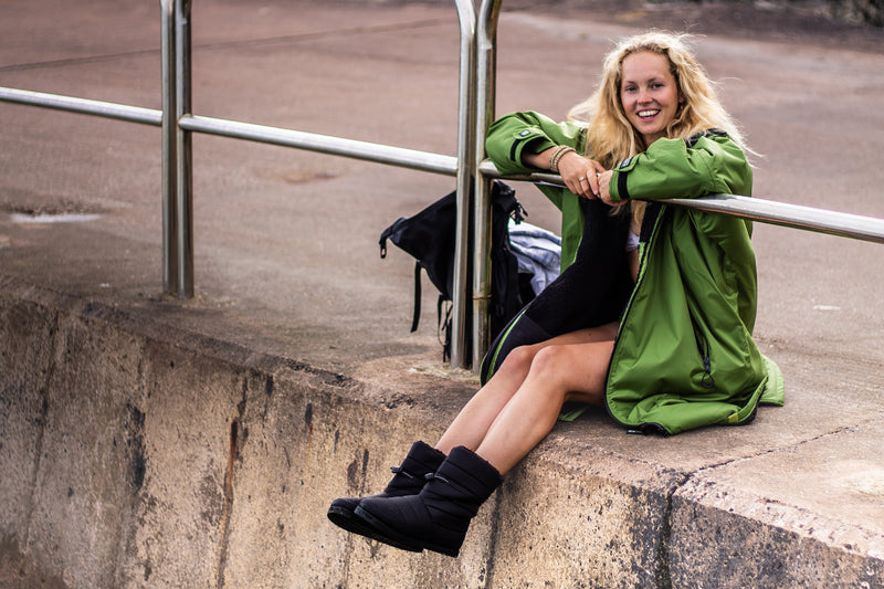 Women sat on a harbour wearing dryrobe thermal boots and a Forest Green dryrobe Advance