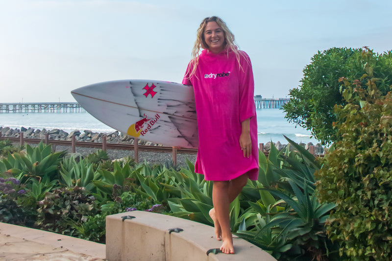 Izzi Gomez holding her surfboard and wearing a dryrobe® Towel Robe