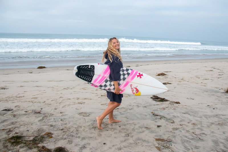 Izzi Gomez holding her surfboard wearing a Towel dryrobe