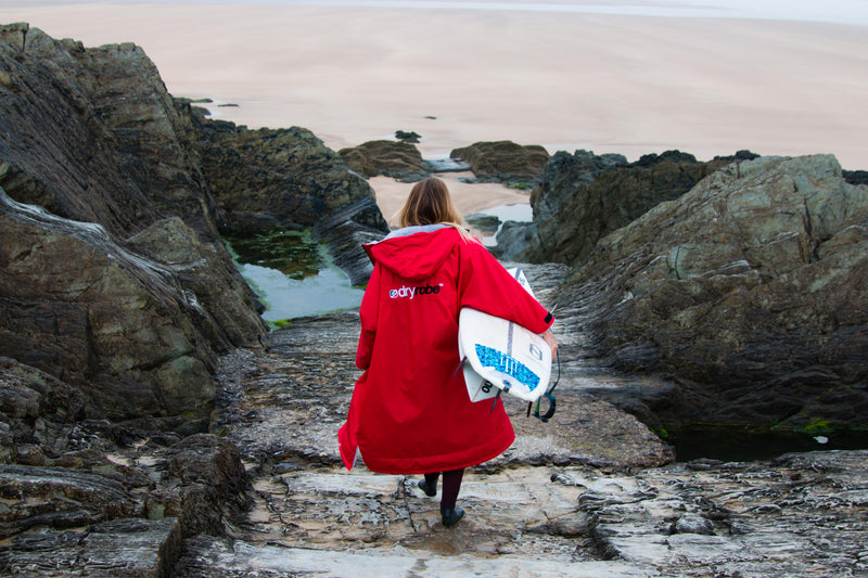 Lucy Campbell holding surfboard on rocks at Woolacombe beach