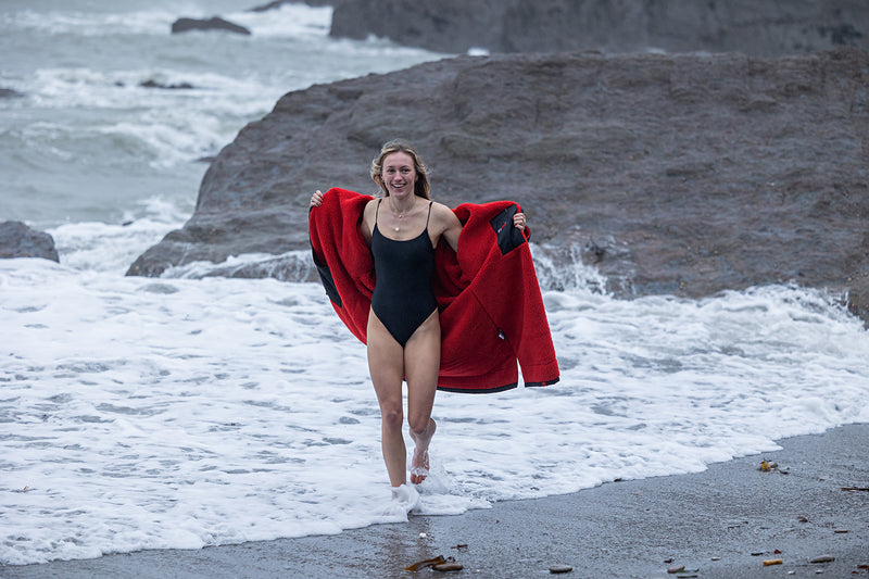 A woman in a swimming costume wearing a dryrobe change robe smiling by the sea