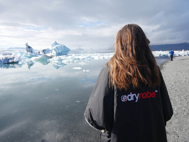 Woman wearing a dryrobe change robe on the edge of an icy lake