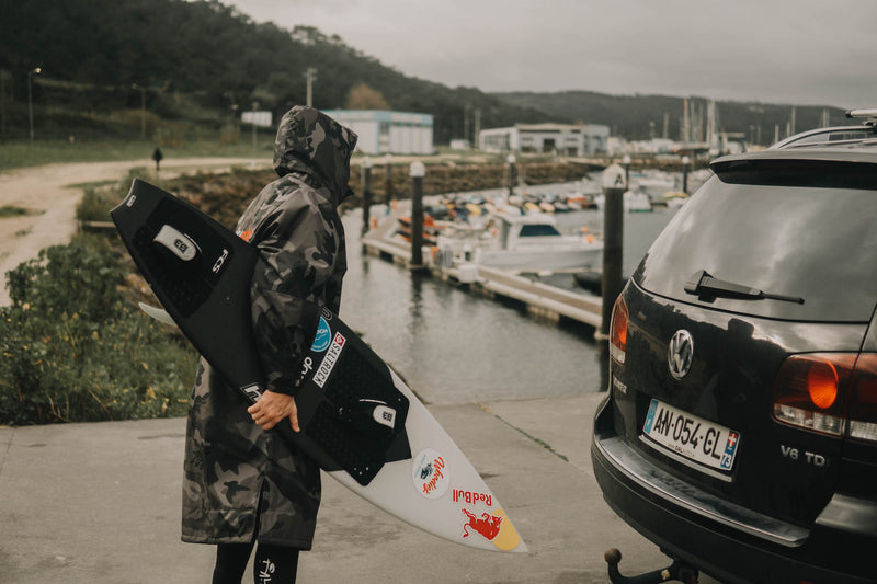 Big wave surfer Andrew Cotton in a dryrobe stood with his surfboard by a car