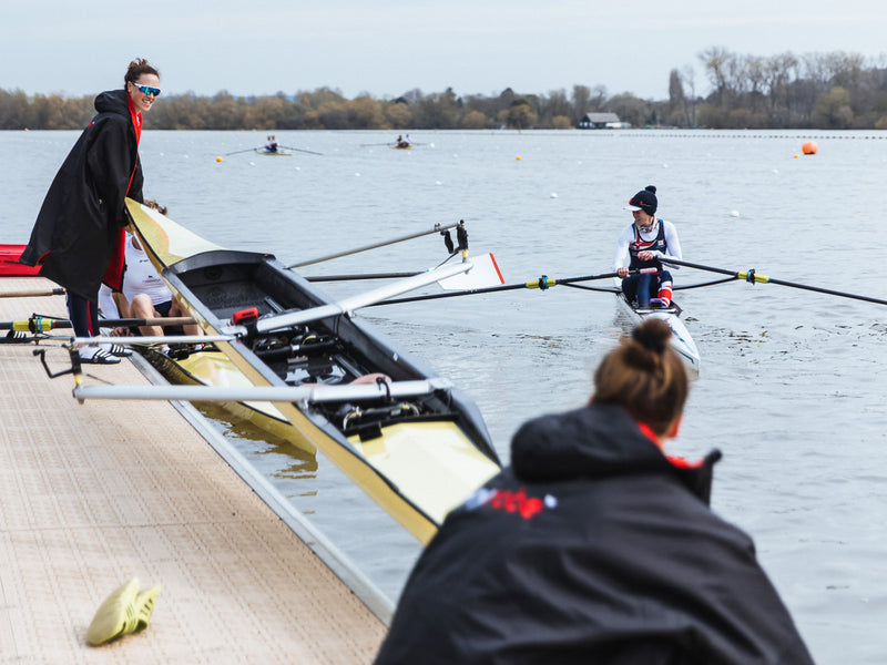 Two British rowers placing a boat in the water and wearing dryrobes