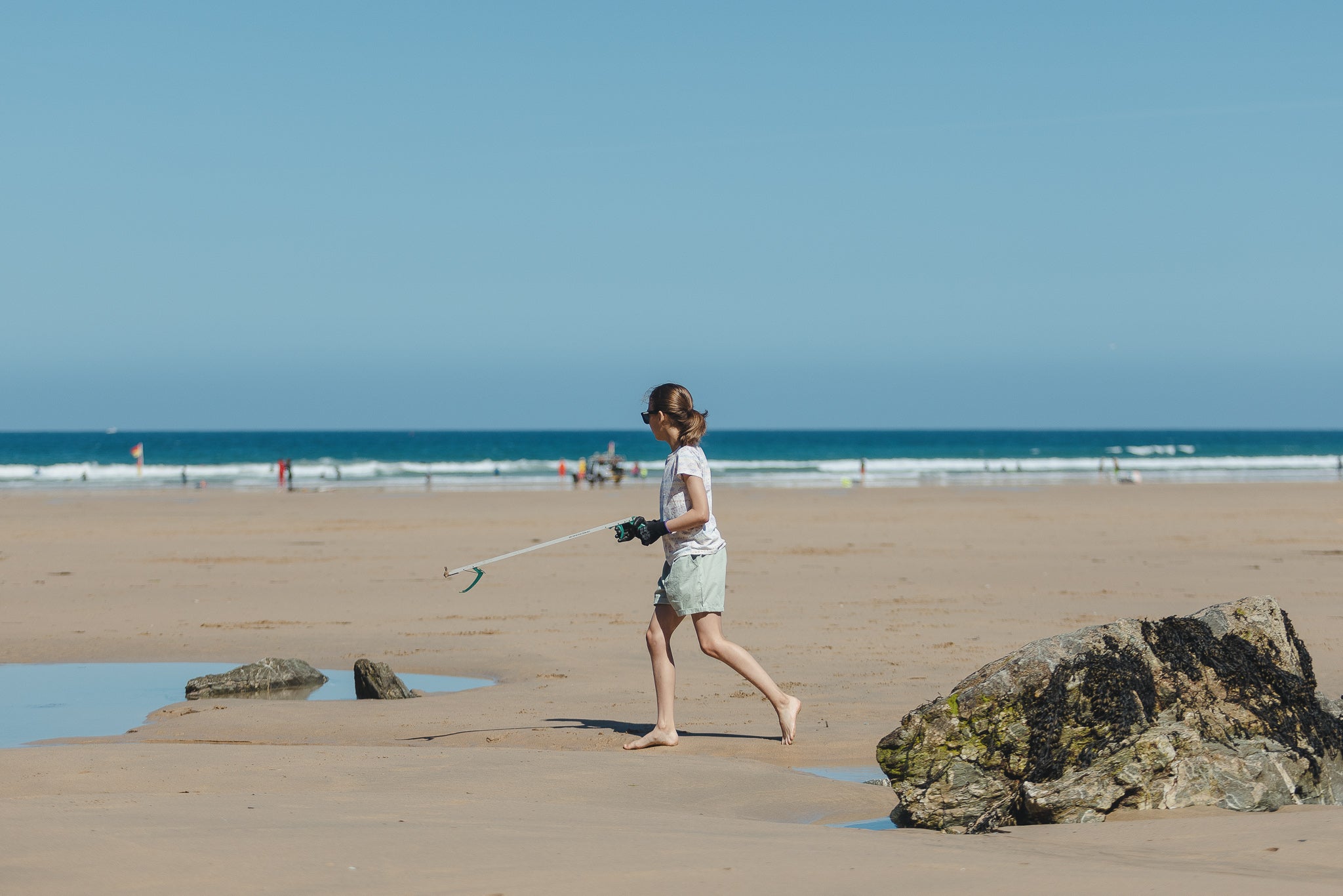 Child walking along the beach holding a litter picker