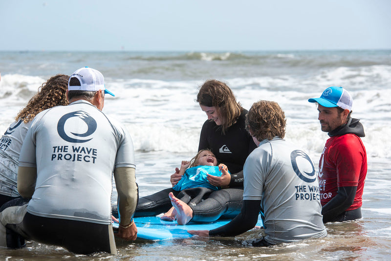 Wave Project volunteers in the sea with a girl on a surfboard