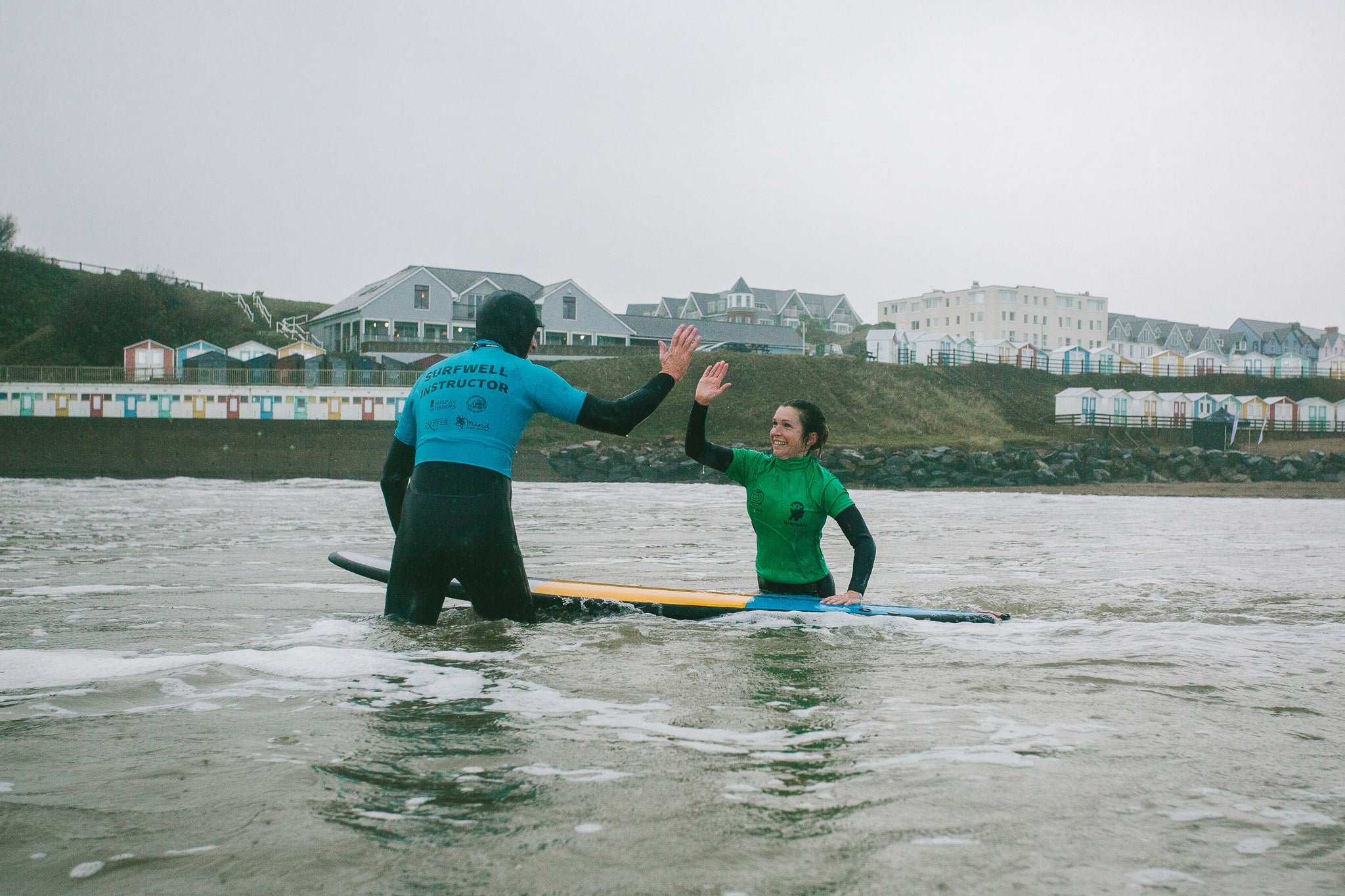 Surfwell participant and a surf therapy instructor giving each other a high-five in the water