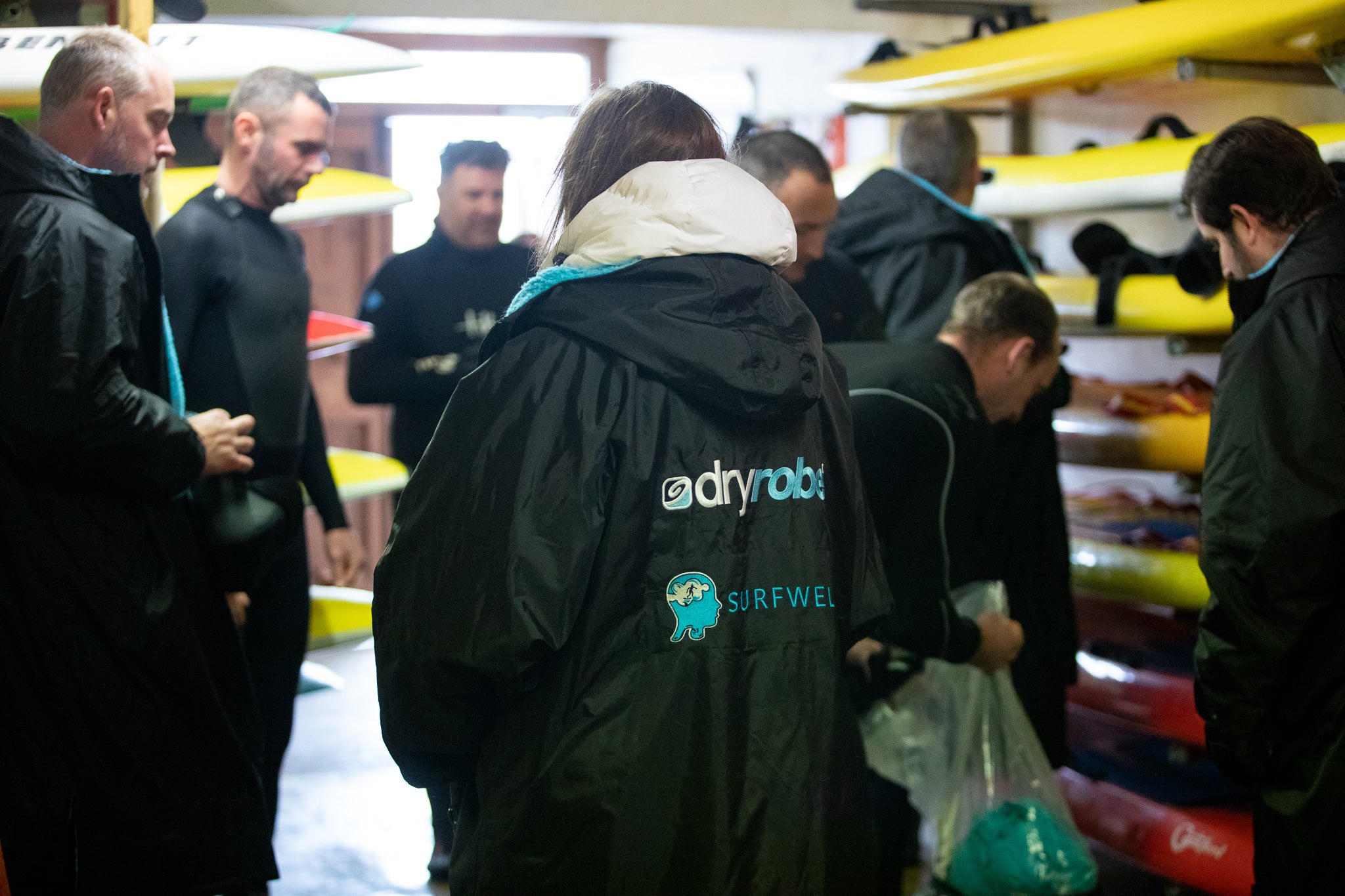 Surfers getting their boards ready indoors wearing dryrobes 