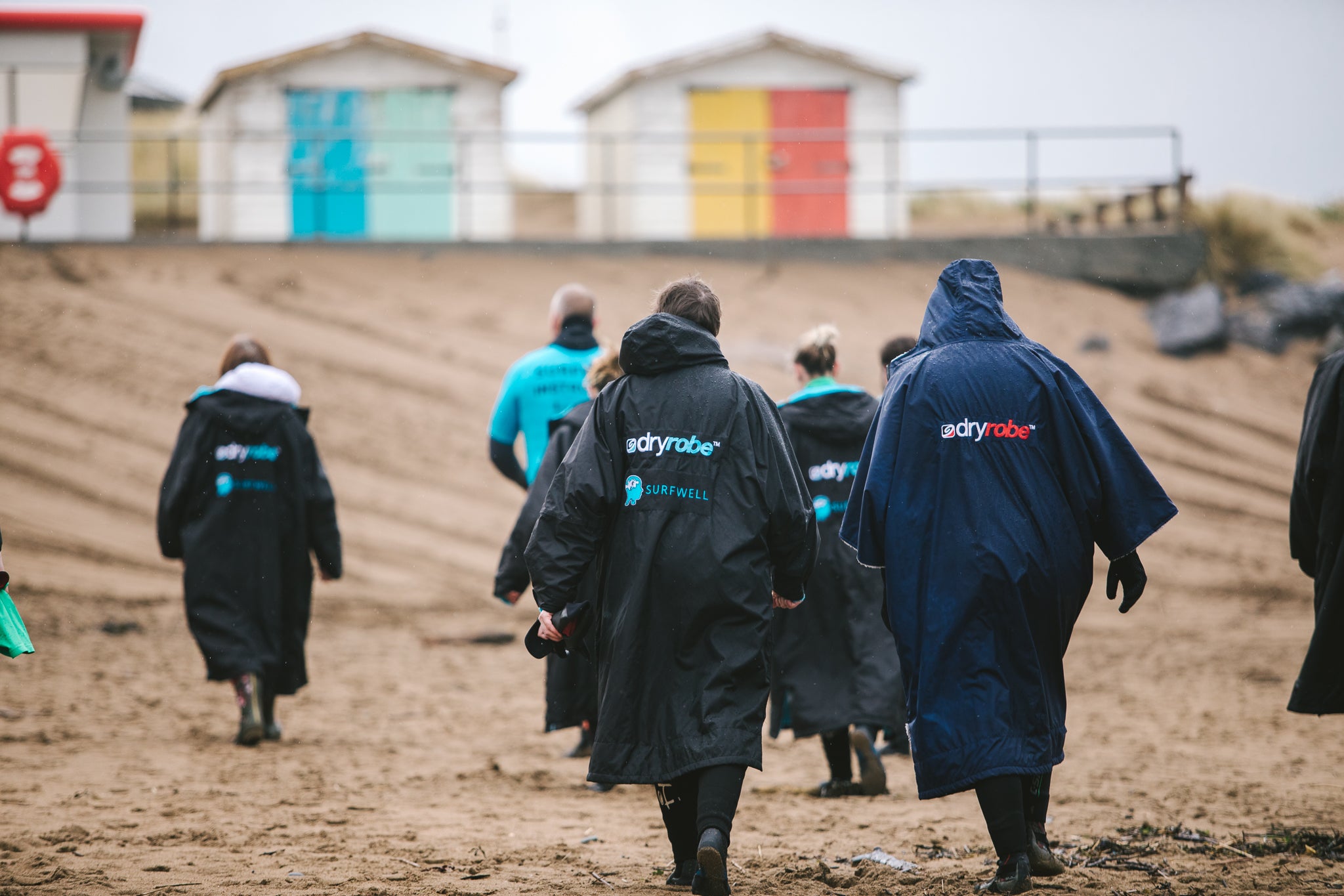 Surfers wearing dryrobes on the beach walking towards beach huts 