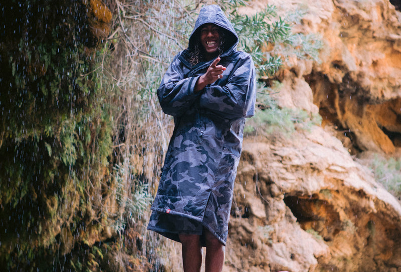 A man wearing a dryrobe under a waterfall smiling