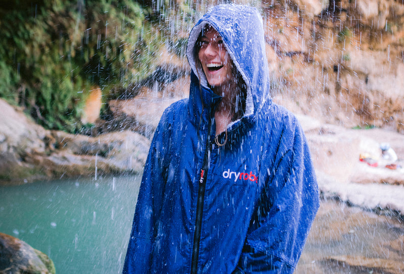 A woman wearing a dryrobe under a waterfall smiling