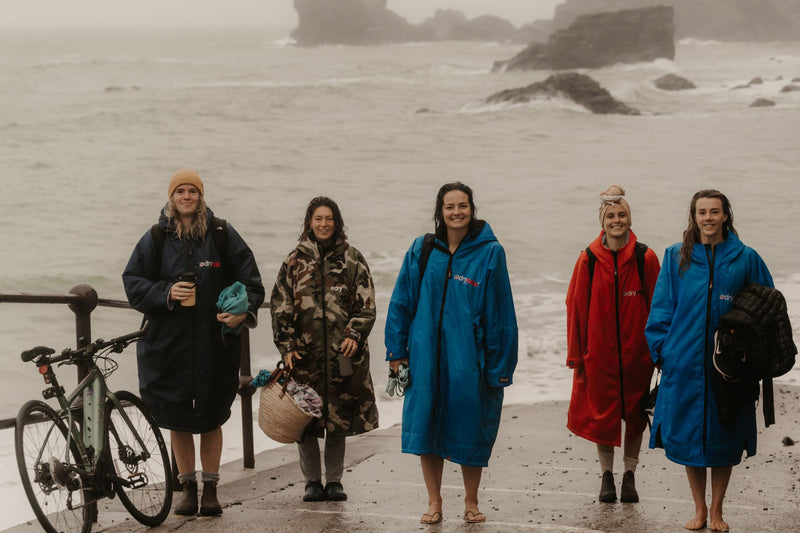 A group of female swimmers wearing dryrobes on the beach