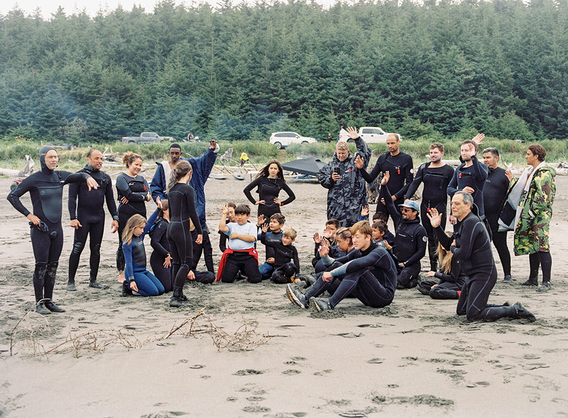 A group of young people on the beach wearing wetsuits and smiling after a surf 