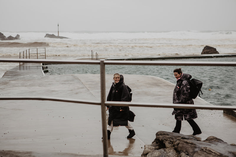 Two women walking to an the sea in dryrobes on a grey day