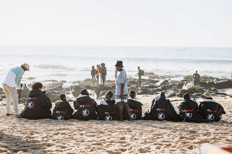 The SNSC crew sat on the beach in a row wearing dryrobes at wsl J Bay