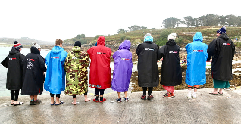 A group of swimmers wearing different coloured dryrobes stood in a line with their back to the camera 