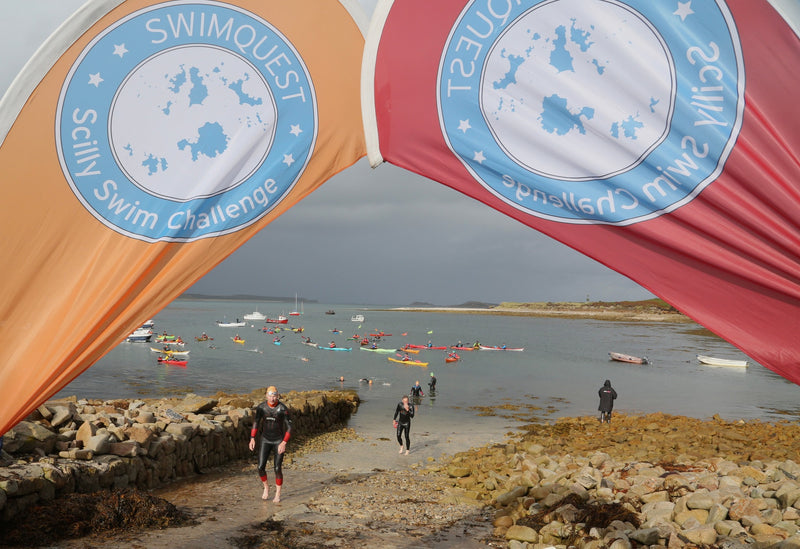 A red and orange Scilly Swim Challenge flags framing a view of the sea 
