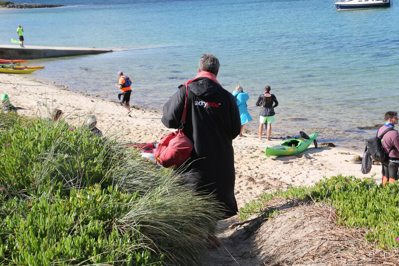 A swimmer in a dryrobe Advance with a swim bag looking at the beach 