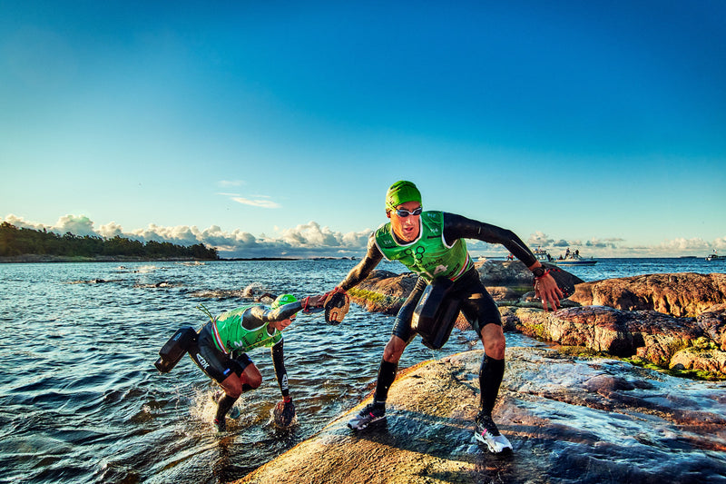 An ÖTILLÖ competitor wearing a green vest helping their team mate up a rock