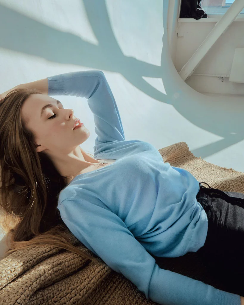 Young woman wearing a light cashmere jumper as sun rays shine on her face.