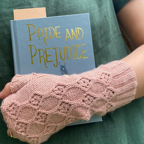 Close up of girl wearing green dress and pink hand knitted fingerless mitts holding a blue Pride and Prejudice book