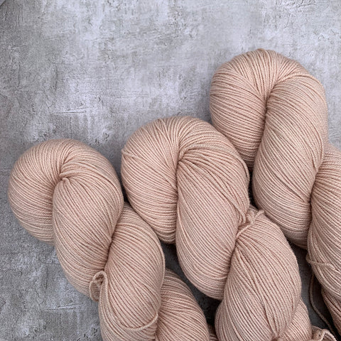 Three light pink skeins of hand dyed sock yarn on a grey marble background