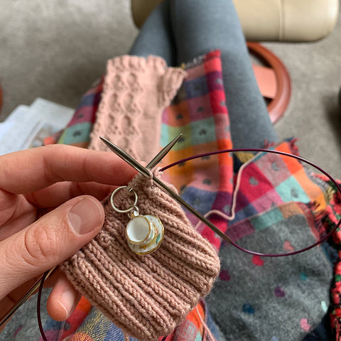 close up hand knitting with a tea cup stitch marker