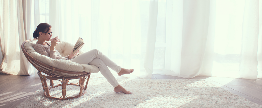 Frau entspannt in einem Stuhl, trinkt CBD-Tee und liest ein Buch