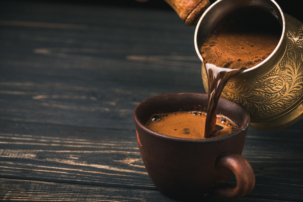 Pouring turkish coffee into vintage cup on wooden background