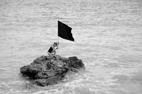 Image of women on a rock in the sea with a flag