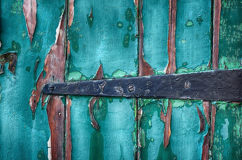 Old damaged green wooden door with a black iron hinge